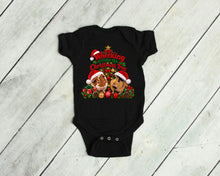 Load image into Gallery viewer, A black baby bodysuit laid flat on a light gray wood plank background. The bodysuit features a festive Christmas graphic with two guinea pigs wearing Santa hats, a Christmas tree, ornaments, and the text 'Wheeking around the Christmas Tree'.