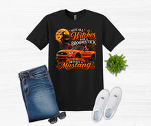 Load image into Gallery viewer, A black graphic t-shirt featuring an orange Mustang car and a witch on a broomstick design, styled in a flat lay with blue jeans, white sneakers, sunglasses, and a small green plant on a white wood background.