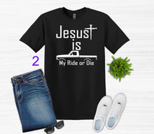 Load image into Gallery viewer, Black t-shirt with 'Jesus is my ride or die' design, paired with jeans, sneakers, and sunglasses on a white background.