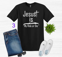 Load image into Gallery viewer, Black t-shirt with 'Jesus is my ride or die' text, paired with jeans, sneakers, sunglasses, and a plant on a white background.