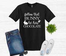 Load image into Gallery viewer, Black t-shirt with 'follow that bunny he has chocolate' text, paired with jeans, sunglasses, and sneakers on a white background.