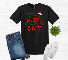 Load image into Gallery viewer, Black t-shirt with 'Dear Santa It Was My Cat' text, jeans, sunglasses, and white shoes on a light background
