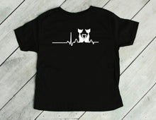 Load image into Gallery viewer, Black t-shirt with a white cat graphic design on a wooden surface