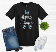Load image into Gallery viewer, Black t-shirt with 'Hippity Hop' text, blue bunny ears, and paw prints, paired with jeans, sneakers, sunglasses, and a plant on a white background.