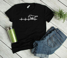 Load image into Gallery viewer, Black t-shirt with a mustang heartbeat graphic design, green tumbler, and blue shorts on a light wooden floor.