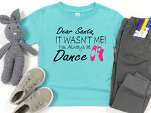 Load image into Gallery viewer, A turquoise graphic t-shirt laid flat with gray pants, a gray crochet bunny toy, and gray sneakers around it on a white background. The shirt has black text reading 'Dear Santa, IT WASN'T ME! I'm Always at Dance' with pink ballet shoes.