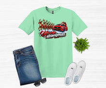 Load image into Gallery viewer, A mint green graphic t-shirt featuring a 'Merry Stangmas' Santa Claus in a red muscle car with reindeer, styled in a flat lay with blue jeans, white sneakers, sunglasses, and a small green plant on a white wood background.