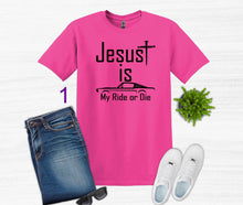 Load image into Gallery viewer, Pink t-shirt with 'Jesus is my ride or die' text, paired with jeans, sneakers, and sunglasses on a white background.
