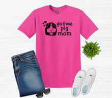 Load image into Gallery viewer, Pink t-shirt with 'guinea pig mom' text, blue jeans, white sneakers, sunglasses, and a small plant on a white background.