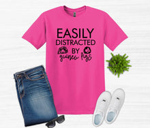 Load image into Gallery viewer, Pink t-shirt with t shirt easily distracted by guinea pigs text, blue jeans, white sneakers, sunglasses, and a plant on a white background