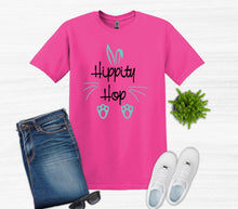 Load image into Gallery viewer, Pink t-shirt with 'Hippity Hop' text, jeans, white sneakers, and sunglasses on a light gray background.