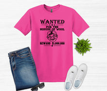 Load image into Gallery viewer, A bright pink graphic T-shirt laid flat on a white wood background, styled with folded blue jeans, white sneakers, sunglasses, and a small green plant. The shirt has a black 'WANTED' poster-style print reading 'FOR THE MISUSE OF WOOL' with a cartoon face and 'REWARD $1,000,000'.