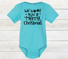 Load image into Gallery viewer, A light blue short-sleeve baby bodysuit with black printed text reading 'We Woof you a Merry Christmas' and paw print accents, displayed flat against a white wood plank background.