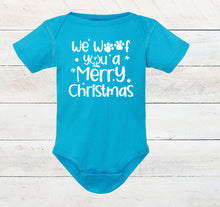 Load image into Gallery viewer, A bright turquoise short-sleeve baby bodysuit with white printed text reading 'We Woof You a Merry Christmas' and paw print details, laid flat on a white wood plank background.