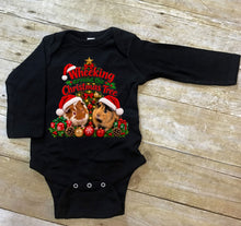 Load image into Gallery viewer, A black baby bodysuit with a festive Christmas graphic featuring two guinea pigs in Santa hats and the text 'Wheeking Around the Christmas Tree', laid flat on a light gray wood plank background.