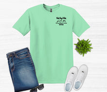 Load image into Gallery viewer, Green t-shirt with text, blue jeans, white sneakers, sunglasses, and a plant on a light gray background