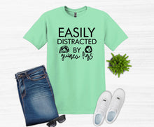 Load image into Gallery viewer, Mint green t-shirt with t shirt easily distracted by guinea pigs text, blue jeans, white sneakers, and sunglasses on a white background