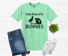 Load image into Gallery viewer, Green t-shirt with bunny graphic and text, paired with jeans, sunglasses, and shoes on a white background.