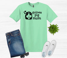 Load image into Gallery viewer, Mint green t-shirt with 'guinea pig mom' text, blue jeans, white sneakers, sunglasses, and a small plant on a white background.