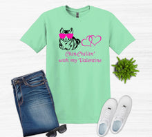 Load image into Gallery viewer, Light green t-shirt with graphic design and text, paired with jeans, sneakers, and sunglasses on a white background.