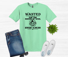 Load image into Gallery viewer, A mint green graphic t-shirt featuring a black 'WANTED' poster design for 'The Misuse of Wool' with a $1,000,000 reward. The t-shirt is styled in a flat-lay arrangement with blue jeans, white sneakers, sunglasses, and a small potted green plant on a white wood-textured background.