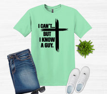 Load image into Gallery viewer, Mint green t-shirt with black I can't but I know a guy text with cross, paired with jeans, sneakers, and sunglasses on a white background.