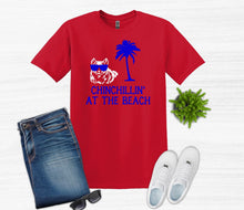 Load image into Gallery viewer, Red t-shirt with 'Chinchillin' at the Beach' design, blue jeans, white sneakers, and sunglasses on a light gray background.