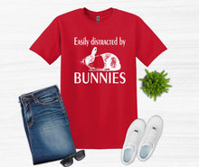 Load image into Gallery viewer, Red t-shirt with 'Easily distracted by Bunnies' text, jeans, sunglasses, and slippers on a white background