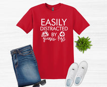 Load image into Gallery viewer, Red t-shirt with 'Easily Distracted by Guinea Pigs' text, jeans, sunglasses, and shoes on a white background