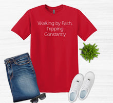 Load image into Gallery viewer, Red t-shirt with text 'Walking by Faith, Tripping Constantly' displayed with jeans, sneakers, sunglasses, and a plant on a white background.