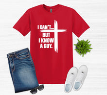 Load image into Gallery viewer, Red t-shirt with I can't but I know a guy text with cross, blue jeans, white sneakers, and sunglasses on a light gray background.