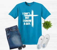Load image into Gallery viewer, Blue t-shirt with I can't but I know a guy text with cross, jeans, white sneakers, sunglasses on a light gray background