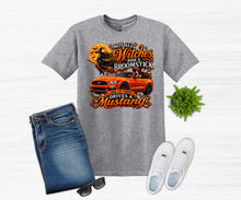 Load image into Gallery viewer, A heather gray graphic t-shirt featuring an orange Mustang car and a witch riding a broomstick design, styled in a flat lay with blue jeans, white sneakers, sunglasses, and a small green plant on a white wood background.