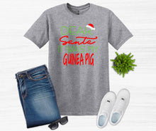 Load image into Gallery viewer, Gray t-shirt with Christmas-themed text, blue jeans, white sneakers, sunglasses, and a plant on a white background.