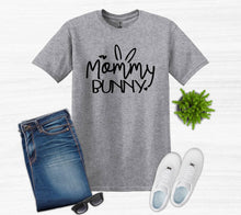 Load image into Gallery viewer, Gray t-shirt with 'Mommy Bunny' text, blue jeans, white sneakers, sunglasses, and a plant on a light gray background.