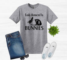 Load image into Gallery viewer, Gray t-shirt with bunny graphic and text, paired with jeans, sneakers, and sunglasses on a white background.