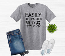 Load image into Gallery viewer, Gray t-shirt with 'Easily Distracted by Guinea Figs' text, paired with jeans, sneakers, sunglasses, and a small plant on a white background.