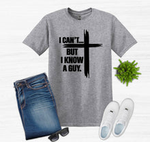Load image into Gallery viewer, Gray t-shirt with I can't but I know a guy text with cross, blue jeans, white sneakers, sunglasses, and a plant on a light gray background.
