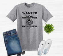 Load image into Gallery viewer, A heather gray graphic t-shirt featuring a black 'WANTED' poster design with the text 'FOR THE MISUSE OF WOOL' and a cartoon character. The t-shirt is styled in a flat-lay arrangement with blue jeans, white sneakers, sunglasses, and a small green plant on a white wood-textured background.