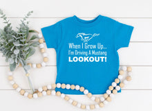 Load image into Gallery viewer, Blue t-shirt with Mustang graphic and text on a white wooden background