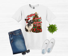 Load image into Gallery viewer, A white graphic t-shirt featuring a rabbit and a Christmas tree design, styled in a flat lay with blue jeans, white sneakers, sunglasses, and a small green plant on a light wood background.